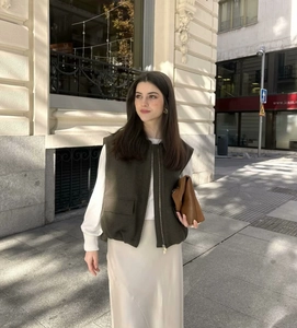Detailed view of women's dark green zip-up vest over white long sleeve top with silk skirt