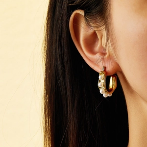Macro view of gold hoop earrings with pearls worn by a model in warm studio lighting