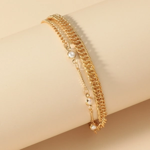 Detail of layered gold curb chain set with pearls on a cylindrical display stand