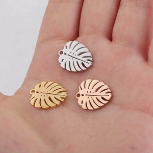 Mirror polished monstera leaf pendants in gold, silver, and rose gold held on palm