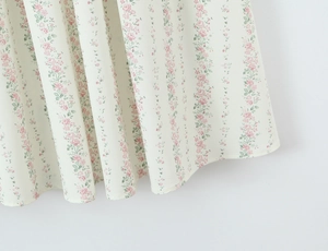Dettaglio dell'abito a fiori bianchi con motivi di rose rosa e tessuto in chiffon plissettato