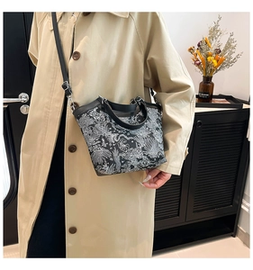 Fashionable black and white printed bucket bag with leather strap worn by a model in a trench coat