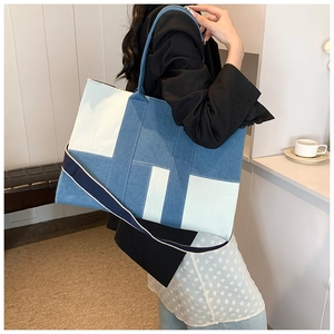 Detailed shot of large denim tote bag with striped shoulder strap on model