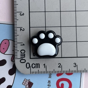 Detail view of 2cm black and white cat paw resin charms with ruler for size reference