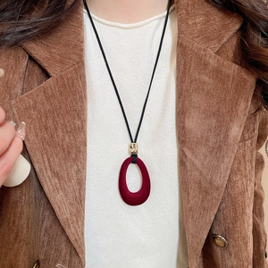 Detail of red flocked oval pendant necklace on black cord over a brown blazer