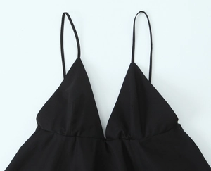 Detail view of black sleeveless V-neck dress featuring thin straps and pleated chest design