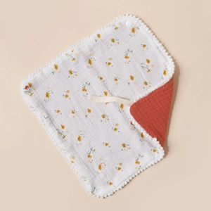 Close-up of cotton baby bib with yellow flower prints and soft white pom-pom trim edge
