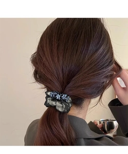 Detail of a dark green mesh scrunchie with blue beaded accents on a low ponytail hair