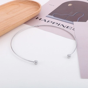 Détail d'un collier ras du cou argenté en C avec des boules lisses sur un plateau en bois