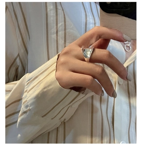Macro detail of the irregular geometric silver saddle ring on finger with beige fabric