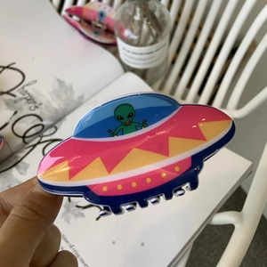 Close-up of a colorful acrylic UFO hair claw clip with a green alien cartoon motif