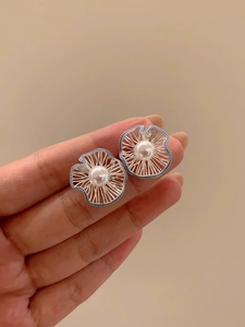 Macro detail of wave flower pearl earrings with blue bead accents held in hand