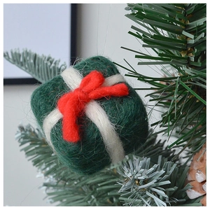 Green wool felt gift box ornament with red bow detail hanging on a Christmas tree branch