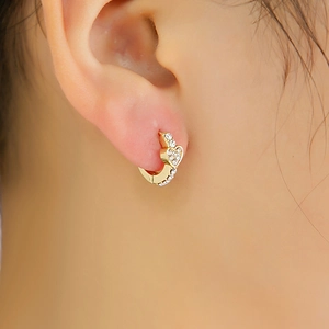 Gros plan de boucles d'oreilles cœur dorées avec strass brillants portées à l'oreille
