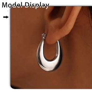 Close-up of a silver-toned teardrop earring with smooth metallic finish on a model's ear