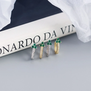 Macro shot of silver and gold clover earrings with green gemstones and white zircon stones