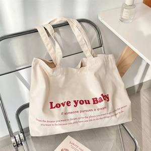 Detail of canvas tote bag featuring red Love You Baby typography on a beige fabric