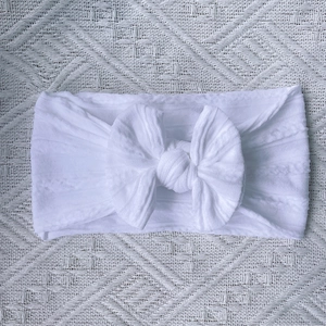 Detail of white nylon baby headband featuring a large bow and cable knit texture