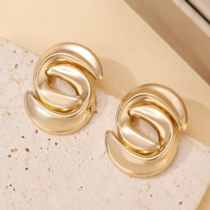 Close-up of golden hollow twisted metal earrings on a textured stone surface