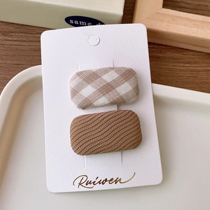 Detail of fabric square hair clips with brown plaid and wavy textures on a card
