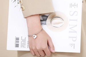 Detail of silver heart charm bracelet worn by a model in a minimalist fashion setting
