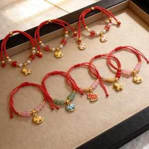 Detail of red braided bracelets with gold horse pendants and pearls on a beige display