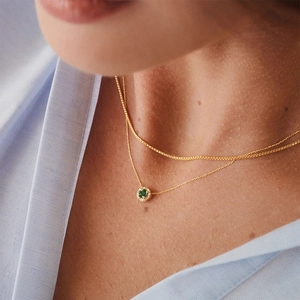 Close-up of a double-layered gold necklace with a round green gemstone on a model