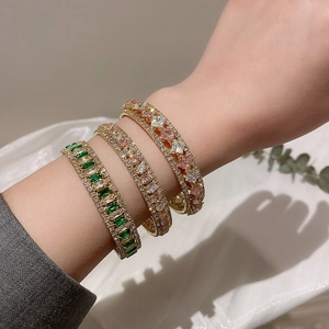 Detailed close-up of three gold-plated bracelets featuring green and pink zircon gemstones