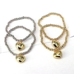 Set of 4 gold and silver beaded bracelets with heart pendants on white background