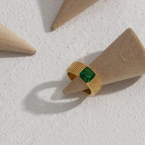 Golden ring with side stripes and square emerald green gemstone on a conical stand