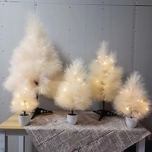 Set of five white feather Christmas trees with warm LED lights on a rustic wood surface
