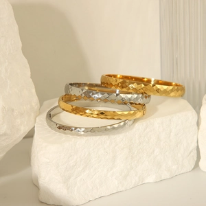 Polished diamond-cut stainless steel bangles in gold and silver on a white stone base