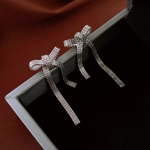 Close-up of silver bow tassel earrings hanging on a luxury jewelry box with velvet