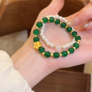 Detalle del juego de pulseras de cuentas de piedra verde esmeralda y perlas en mano