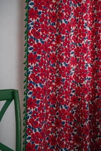 Close-up of red cotton linen curtains with blue floral patterns and green fringe tassels