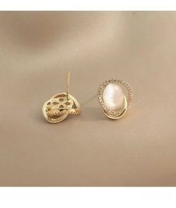 Close-up of golden cat-eye opal stud earrings with diamond halo on silk fabric