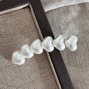 Detail of sweet cream white resin heart hair clip with pearl luster on a beige display tray