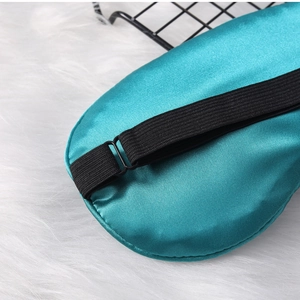 Detail of teal satin sleep mask featuring an adjustable black elastic strap on white plush