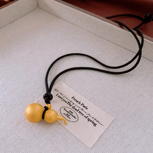 Detail of a matte gold gourd pendant with a black leather cord on a light tray