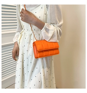 Detailed view of an orange quilted crossbody bag with a metal chain strap on a model