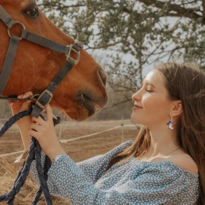 Detail of blue cowboy boot earrings with zircon accents worn by model in a natural setting