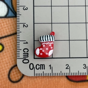 Macro shot of a 2cm mini red resin Christmas stocking charm next to a measuring ruler