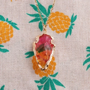Detail of gold arrow pendant with pink and orange gradient crystal on linen surface