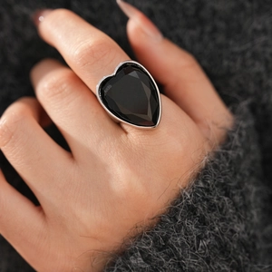 Detailed view of oversized heart-shaped black stone ring on grey sweater