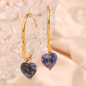 Macro view of gold heart earrings with blue marble stone on a clear glass rim