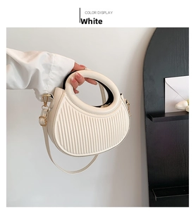 Detail of white pleated handbag with circular cutout handle and gold hardware buckles