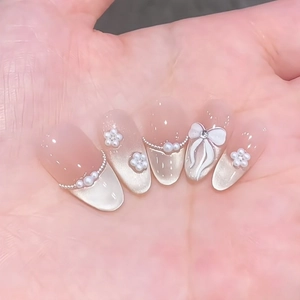 Pink gradient cat-eye press-on nails with 3D bows and pearl chains on almond shape