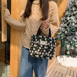 Detail of embroidered daisy canvas tote bag held by model in a cozy winter setting