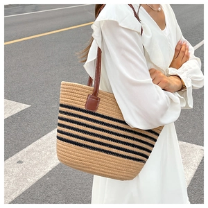 Foto lifestyle di una grande borsa tote in paglia a righe nere e manici in pelle marrone