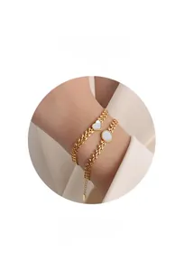 Macro detail of two 18k gold-plated bracelets featuring white mother of pearl heart charms